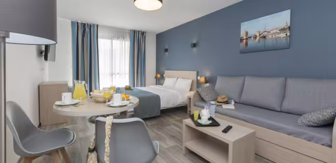 Appartement avec lit double, canapé, table basse, table avec petit-déjeuner et deux chaises.